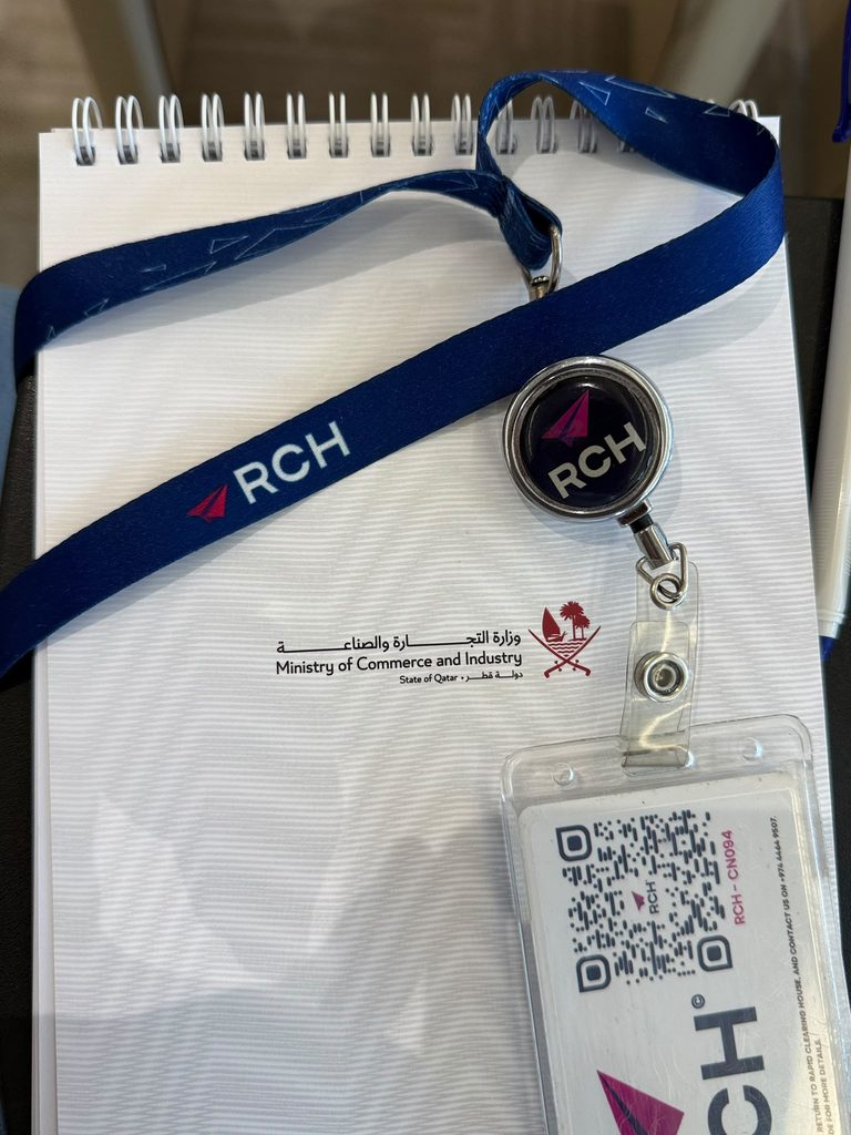 RCH Qatar branded lanyard and participation badge displayed alongside a Ministry of Commerce and Industry notebook.
